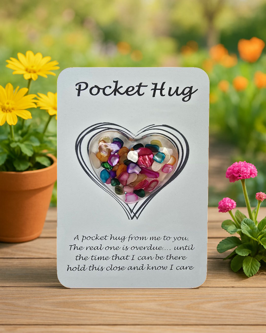 'Pocket Hug' presentation card with resin heart design containing multicoloured crystals on a wooden surface.